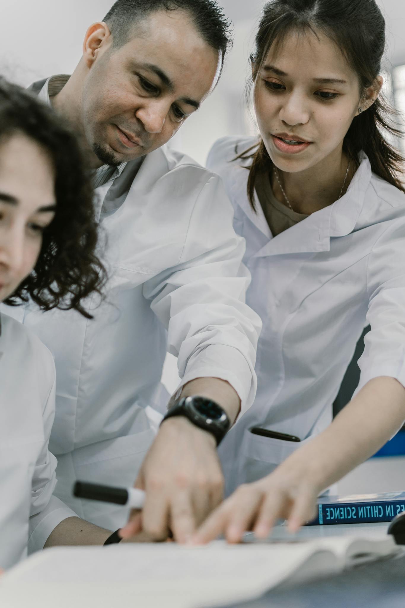 A diverse group of professionals work on a science project, focusing on a book.